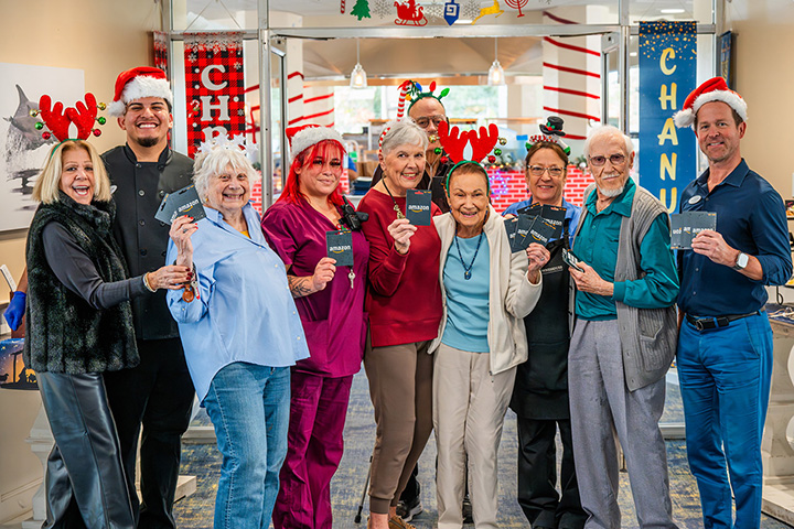 Ventura Townehouse residents and staff wearing Santa hats and holding gift cards for the Teddy Bear Cares Foundation's Annual Toy Drive