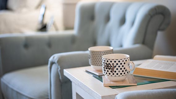 Close up shot of a grey club chair and side table two cups of tea and a book on it