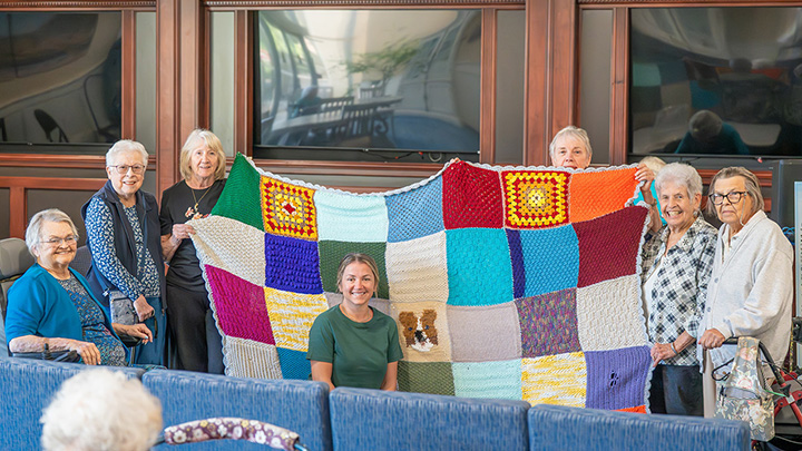 Members of our knitting group shown holding up the handmade quilt presented to Sarah, seated in front, the wife of our Chief Engineer Steve.